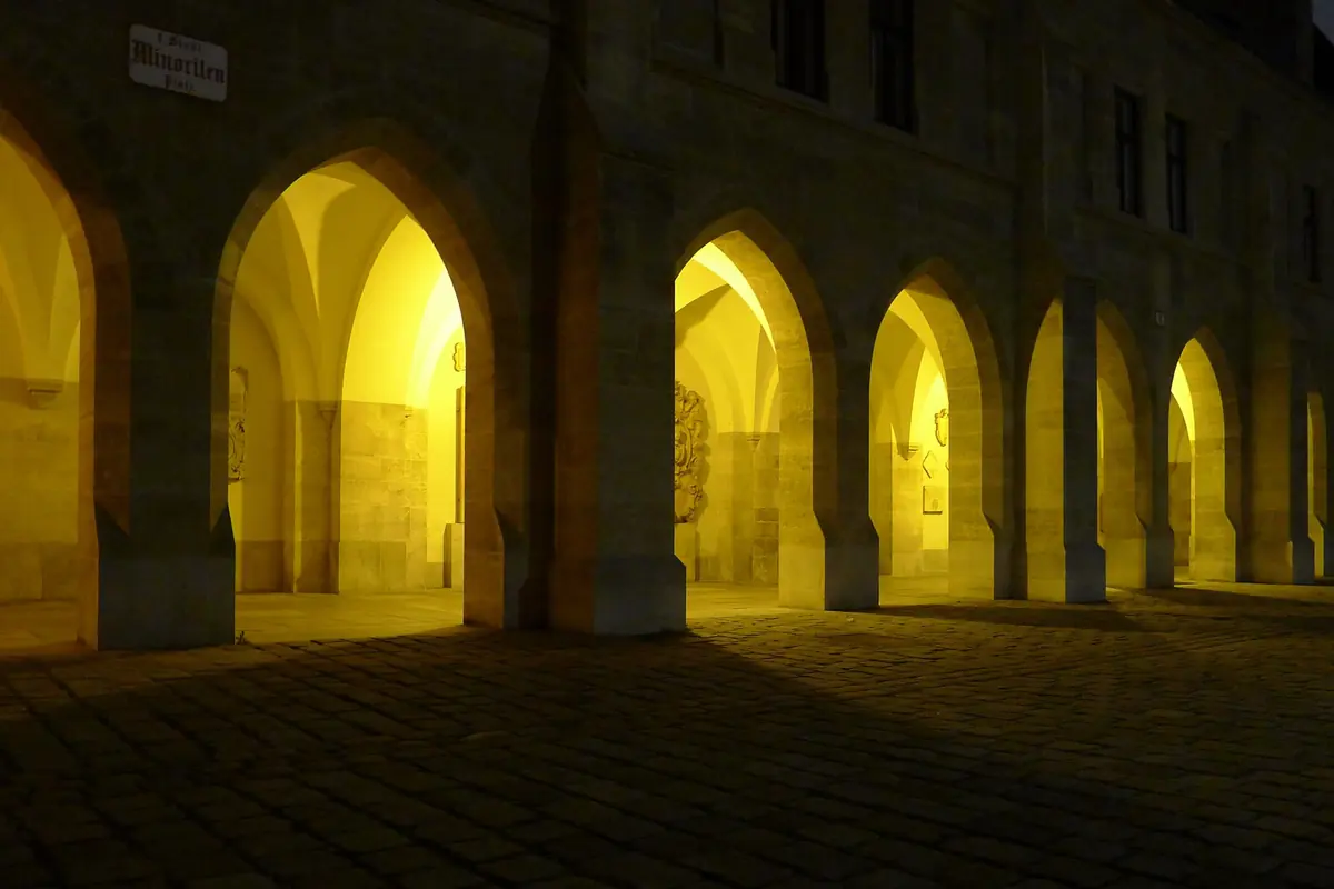 Il portico accanto alla chiesa di notte, con una fila di archi in pietra a sesto acuto illuminati dall’interno da una calda luce gialla.