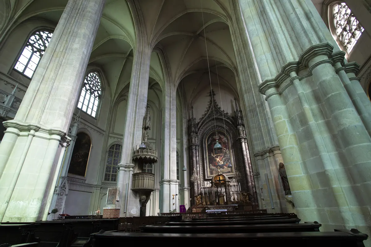 La navata della Minoritenkirche con alte pilastri verde pallido che salgono verso volte a crociera e l'altare maggiore neogotico in fondo.